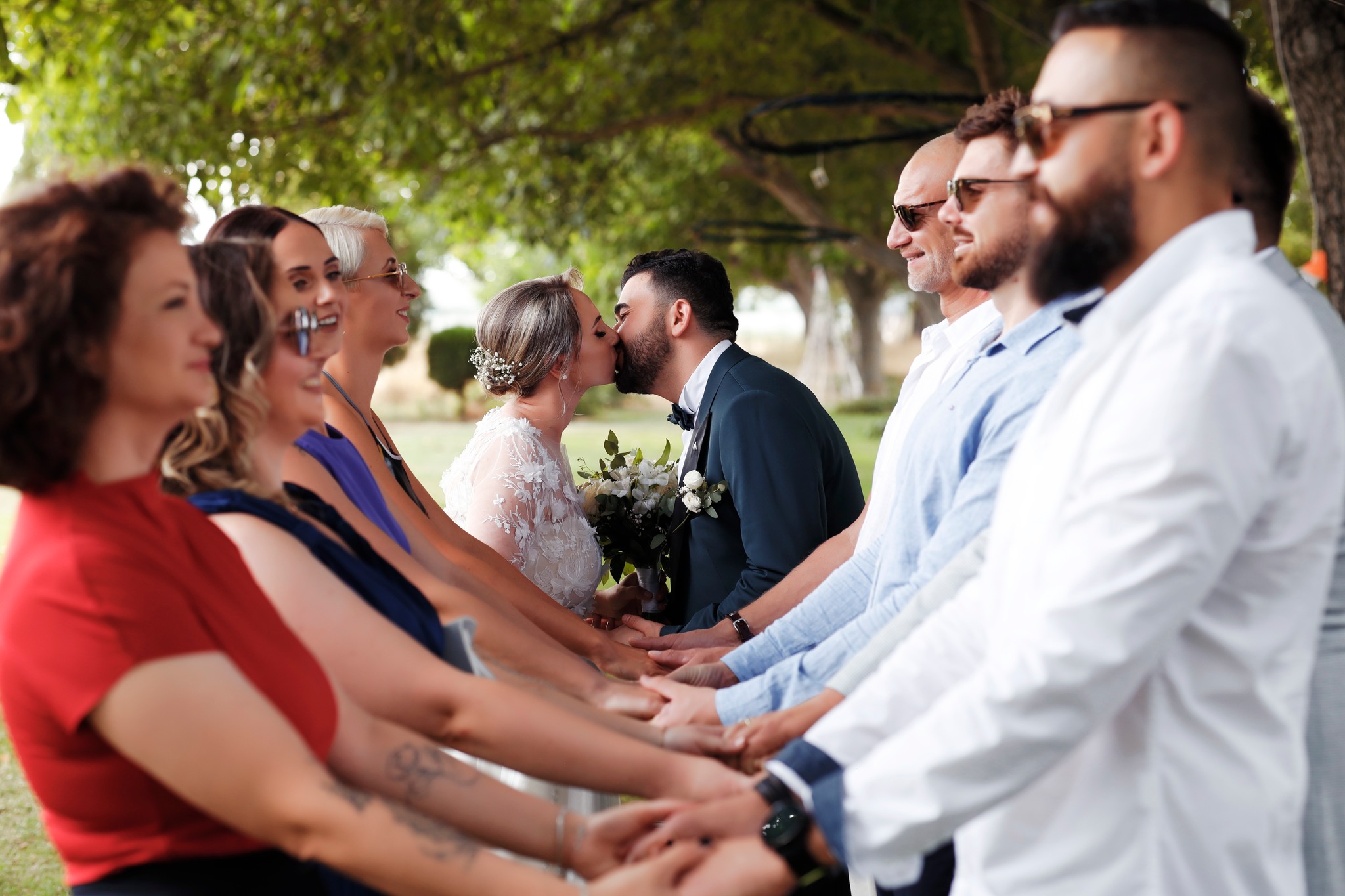Младоженци се бакнуваат опкружени со гости, церемонија на отворено
