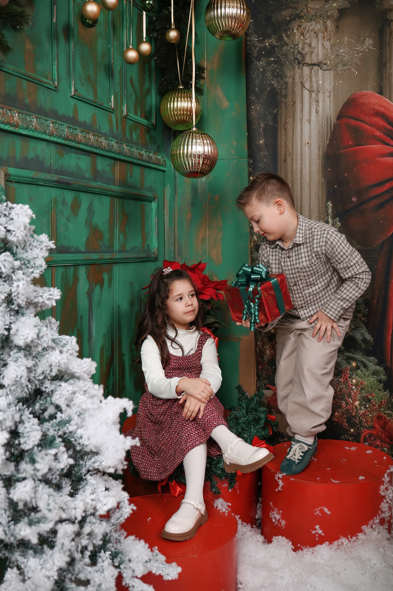 Деца со подарок крај зелена врата со Божиќна декорација