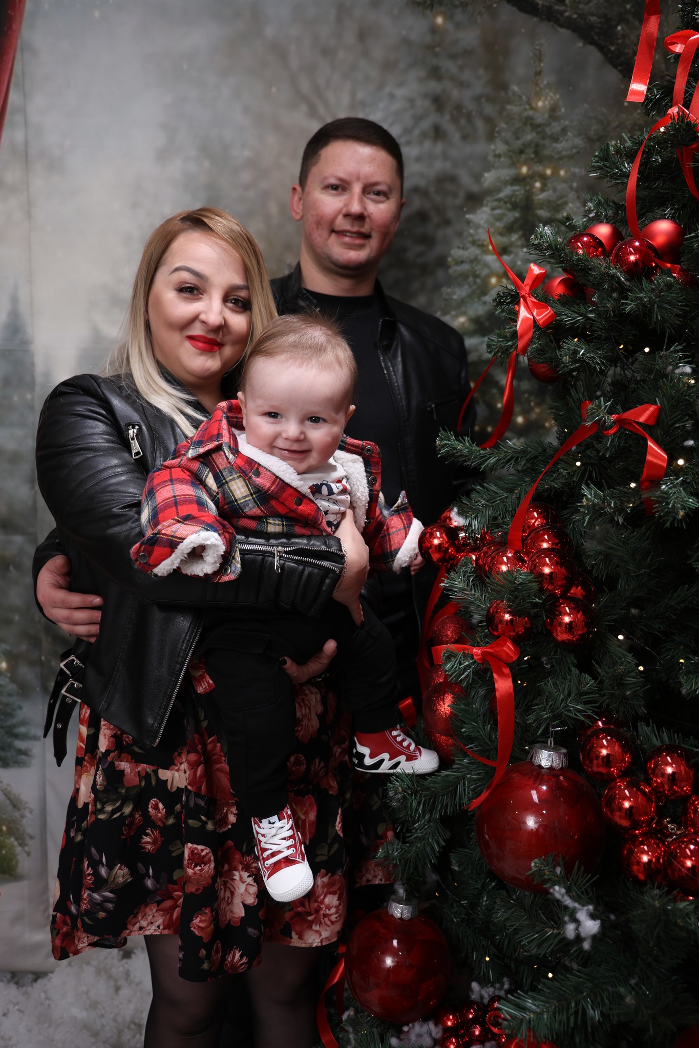 Млада фамилија со бебе крај украсено Божиќно дрво