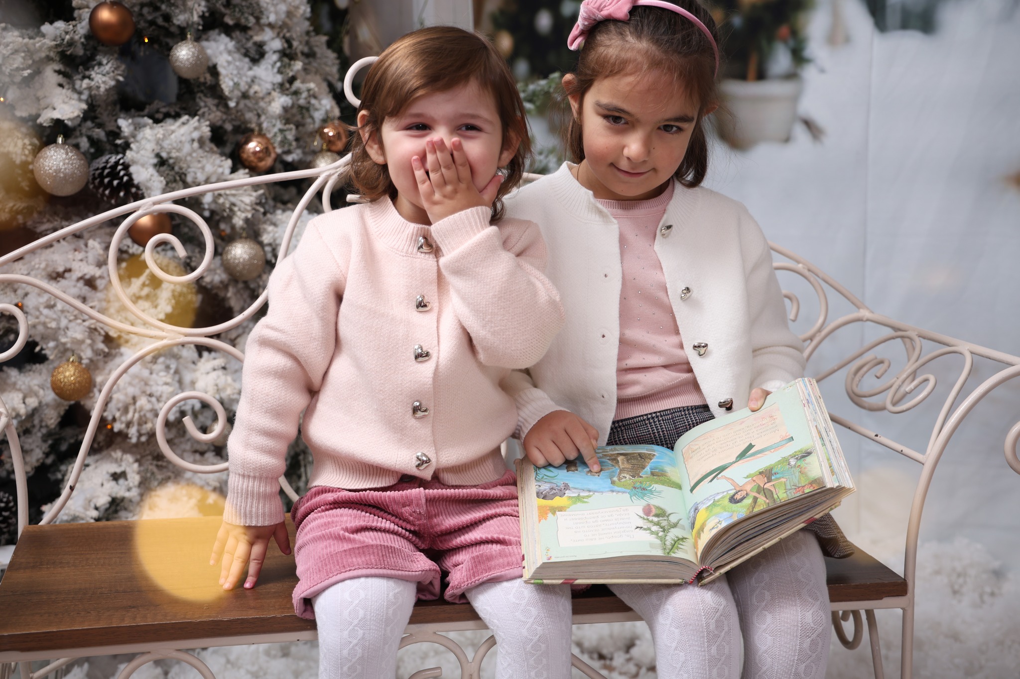 Две мали девојчиња читаат книга на клупа во Божиќна декорација